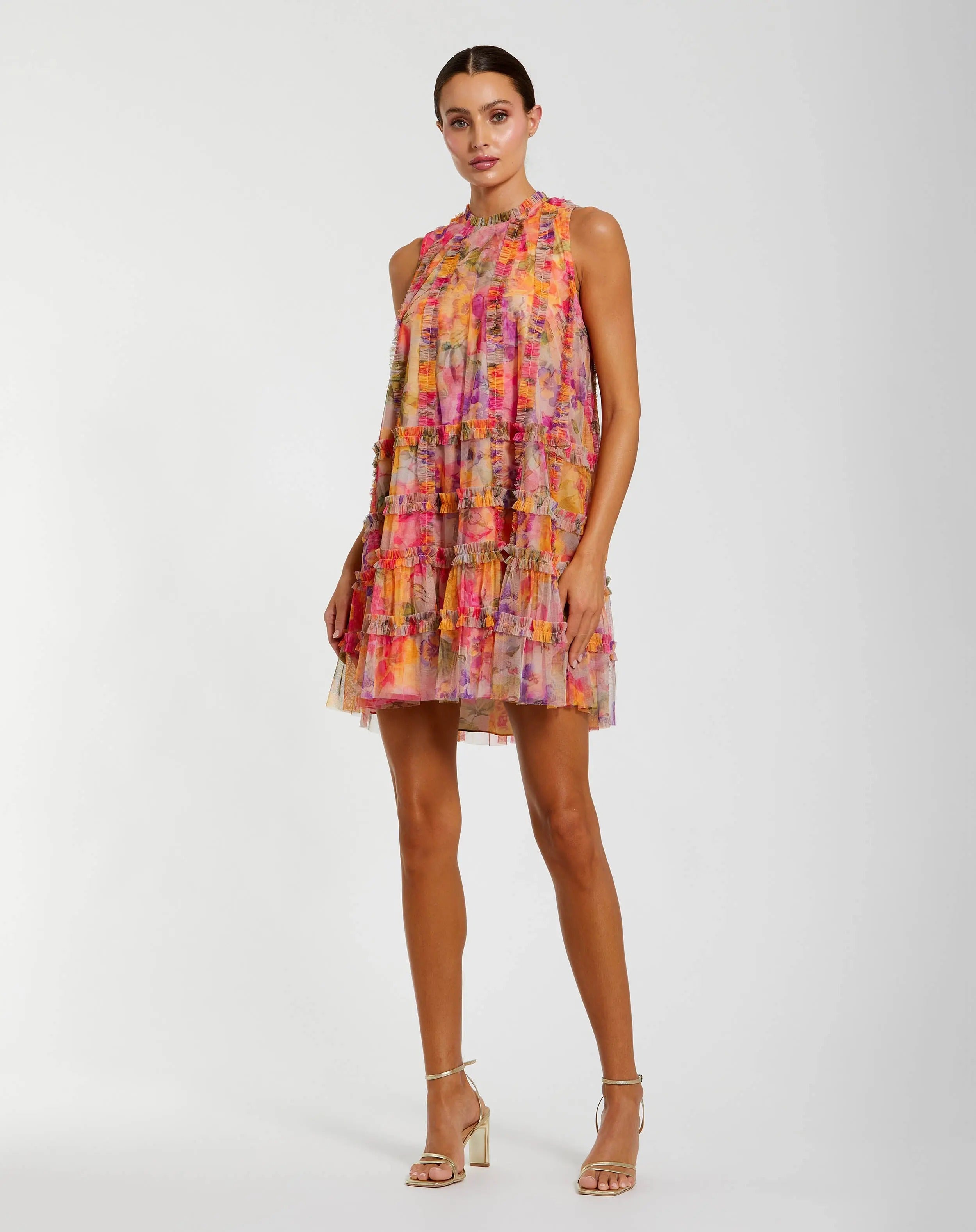 A woman wearing the Mac Duggal 8488 Short Party Dress in Multiโa sleeveless mini with a ruffled silhouette and vibrant floral patternโpairing it with strappy high-heeled sandals against a plain background for a chic, signature look.